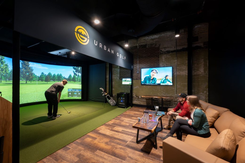 two people watch man using golf simulator